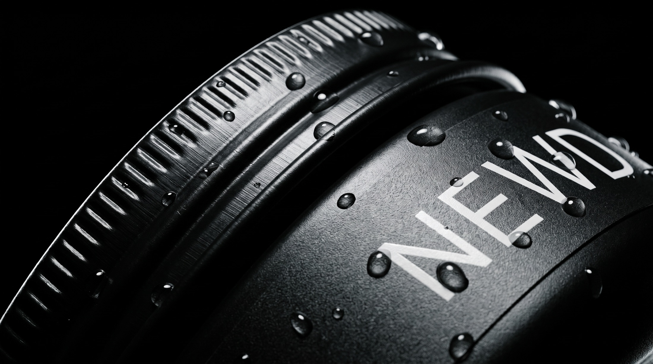 Extreme macro of the NEWD tin's knurled lid with water beading on matte black metal